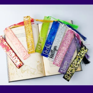 Nine personalised glitter resin bookmarks in assorted colours arranged around an open book, each with a matching tassel