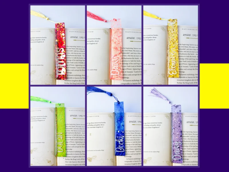 Six personalised glitter resin bookmarks in red, pink, yellow, green, blue and lilac arranged in a neat grid on an open book with matching tassels.
