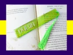 Green glitter bookmark personalised with the name Dylan, placed across the pages of an open book with a bright green tassel
