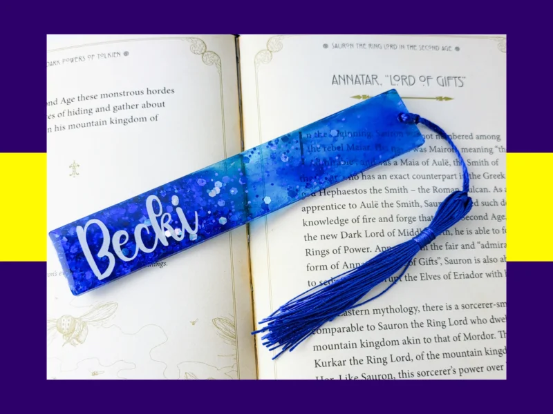 Blue glitter bookmark personalised with the name Becki, displayed on an open book with a matching blue tassel.