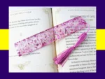 Pink glitter bookmark personalised with the name Daisy, shown across the pages of an open book with a matching pink tassel.