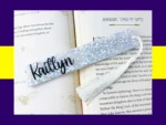 White Silver star glitter bookmark personalised with the name Kaitlyn, resting on an open book with a white tassel.