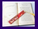 Red glitter personalised bookmark with the name Tomas, displayed on an open book with a gold tassel.