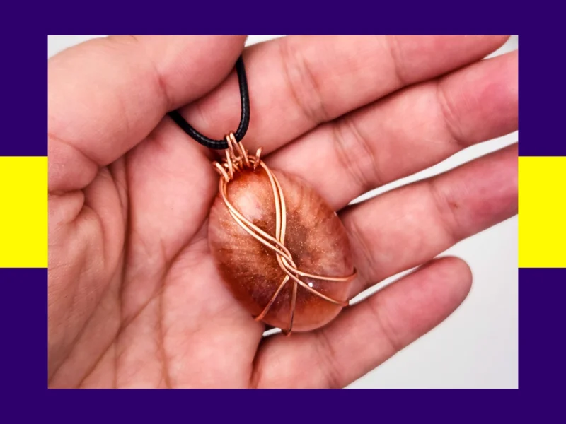 Shimmery copper-tone oval resin pendant with copper wire wrapping displayed in hand – handcrafted jewellery piece