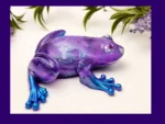 Handmade Aqua Purple Frog resin ornament with purple body, blue feet, and translucent shimmering details, shown on a white background with flowers.