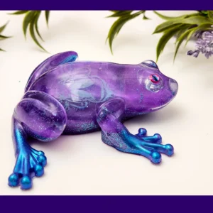 Handmade Aqua Purple Frog resin ornament with purple body, blue feet, and translucent shimmering details, shown on a white background with flowers.