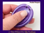 PP-Real-Photo Pocket Peepers purple oval fidget pebble held between the thumb and fingers, showing how it’s used for grounding or sensory comfort