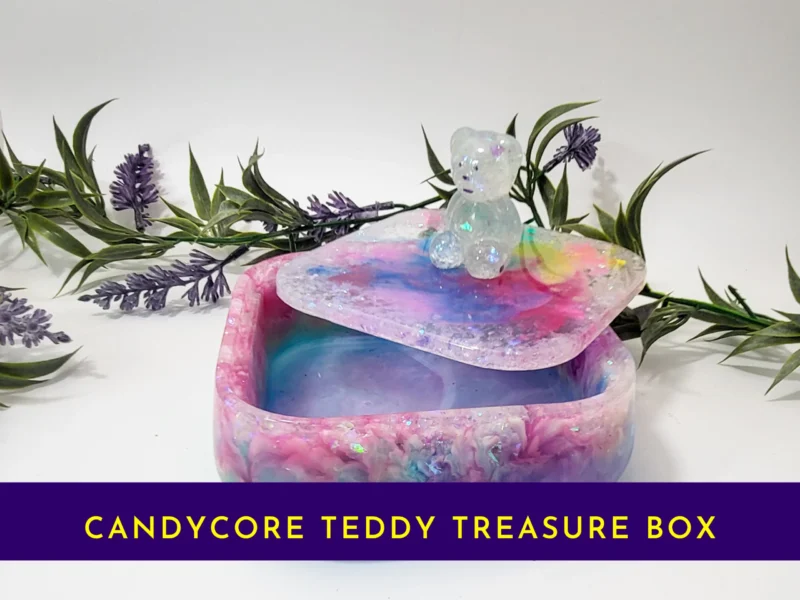 Open pastel rainbow resin treasure box with teddy-topped lid resting on the rim; banner text reads “Candycore Teddy Treasure Box”.
