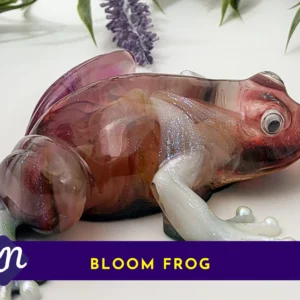 Side view of the Bloom Frog resin sculpture with a marbled burgundy/amber body and pearly legs; a purple banner along the bottom reads “BLOOM FROG” with a small KN logo.