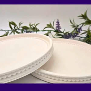 wo white Pearl Rim Round Trays photographed at an angle, showing the beaded edge detail with faux greenery behind.