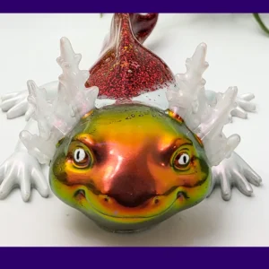 Fire axolotl with iridescent gold-green face and red glitter back on a white background with greenery, framed by a purple border.