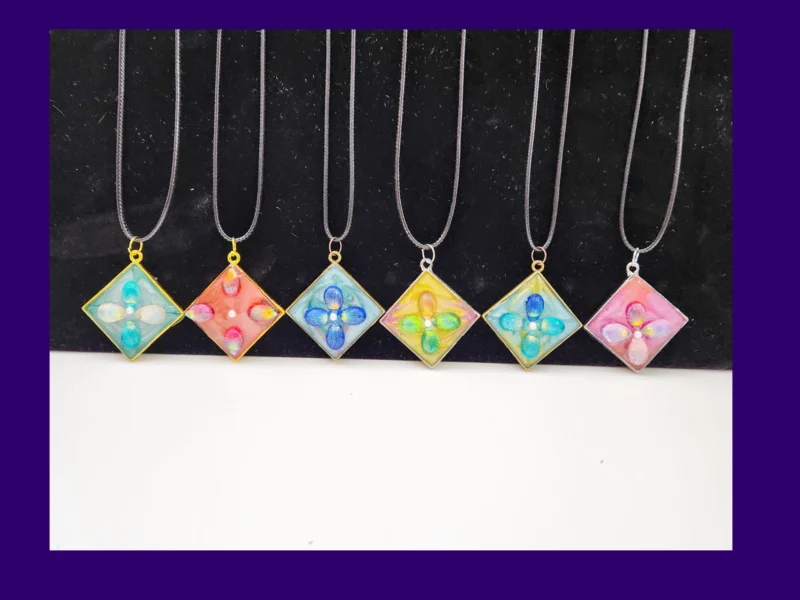 Six one-of-one square resin pendant necklaces lined up on cords, showing different colour designs.