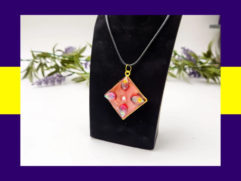 Red-toned square resin petal pendant necklace displayed on a black jewellery stand.