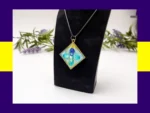 OOO-UVR-001_012 Teal square resin petal pendant necklace displayed on a black jewellery stand