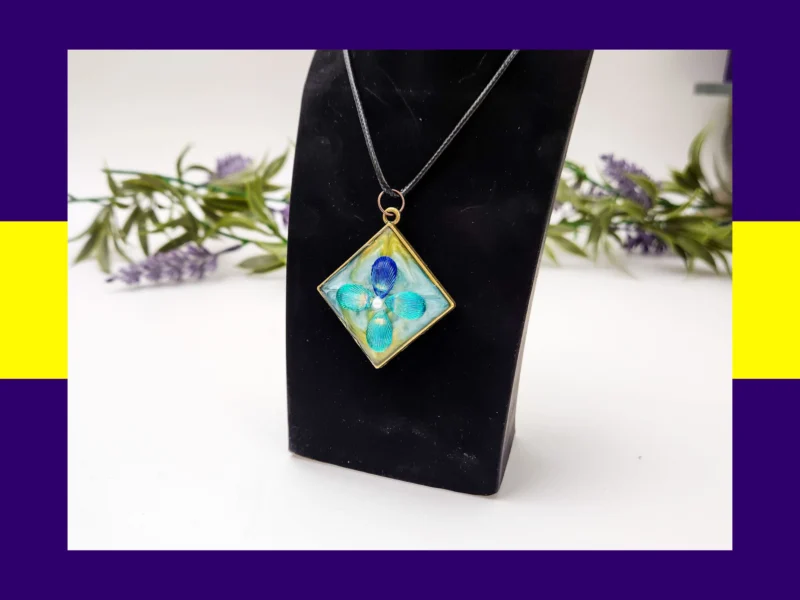 OOO-UVR-001_012 Teal square resin petal pendant necklace displayed on a black jewellery stand