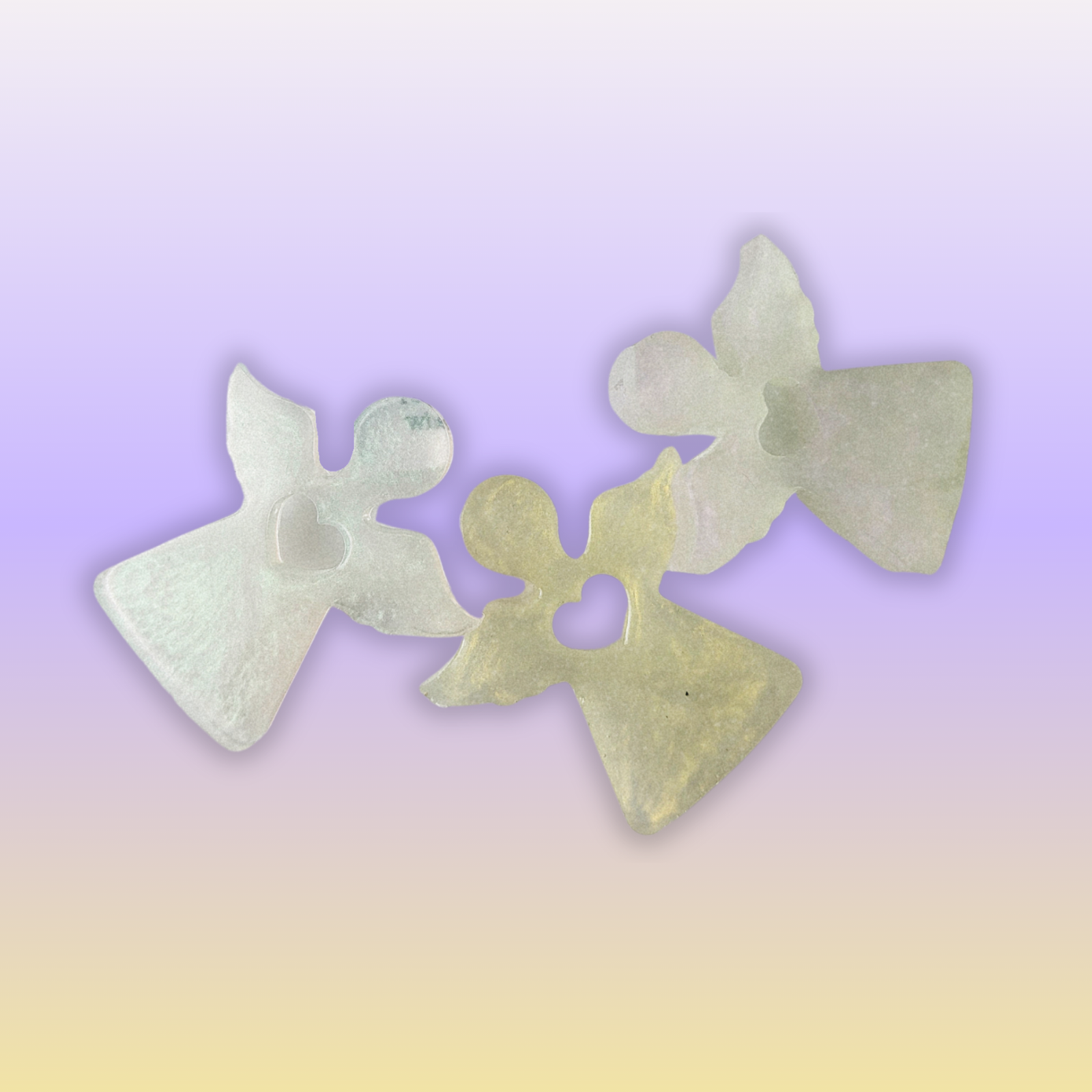 Three handmade resin guardian angel keepsakes with heart detail on a warm oat background.