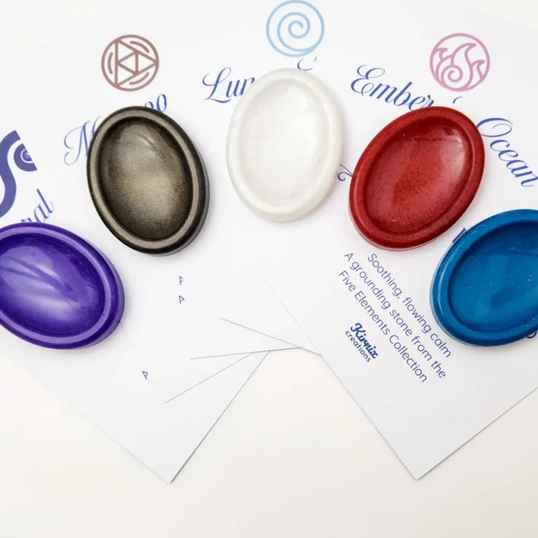 Five oval resin sample stones in purple, black-gold, white, red and blue displayed on branded Kirnix Creations Five Elements Collection cards.
