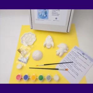 Paint your own space kit laid out on yellow background with paints brushes and instructions