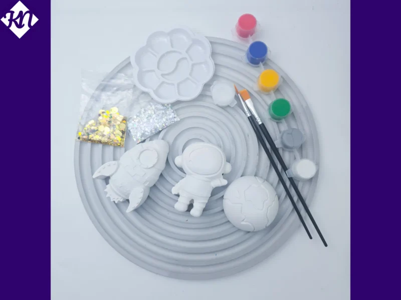 Space craft kit arranged on grey tray with paints brushes glitter and plaster shapes