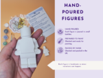 Hand holding a white plastic figure kit with glitter and paint supplies; instruction sheet visible, right side shows a purple infographic panel that reads 'HAND-POURED FIGURES'.