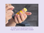 Close-up of hands painting a small craft with yellow paint; paint-splattered fingers.