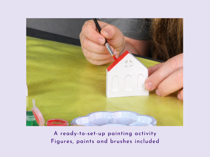 Child’s hand paints a small white ceramic house with a red roof using a fine brush in a craft project.