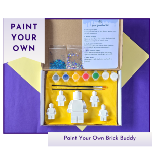Hero product image showing a boxed paint your own brick buddy kit with two blank figures, paint pots and instructions