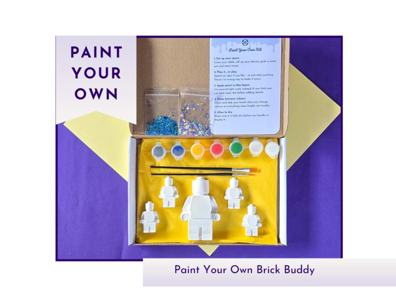 Hero product image showing a boxed paint your own brick buddy kit with two blank figures, paint pots and instructions