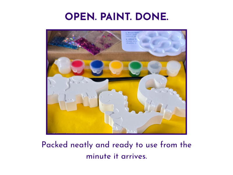 : Open dinosaur craft kit laid out neatly with blank figures, paints, glitter, palette and instructions