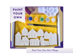 Paint your own mini village kit showing white house figures, paints, brush, palette and kit packaging on a yellow background.