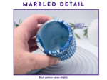 Close-up of a hand holding a blue marbled cupcake liner, highlighting its ridged, glossy interior.
