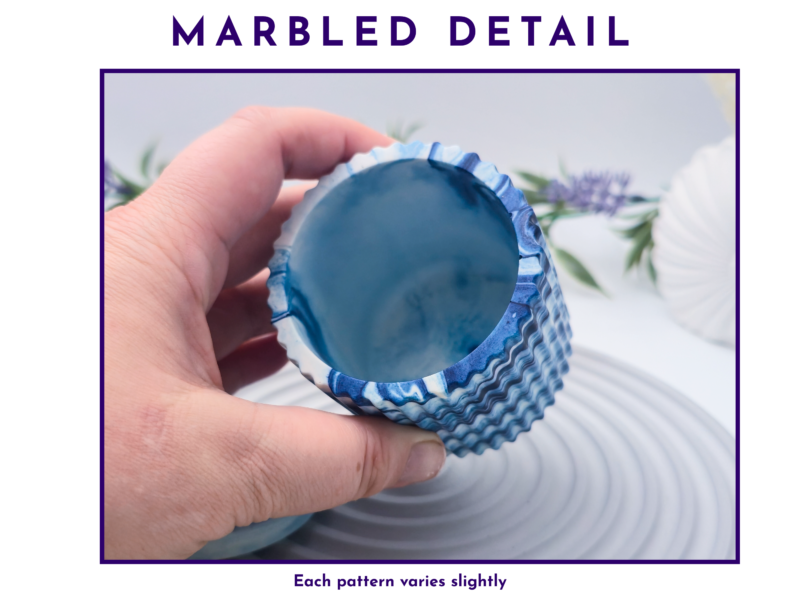 Close-up of a hand holding a blue marbled cupcake liner, highlighting its ridged, glossy interior.