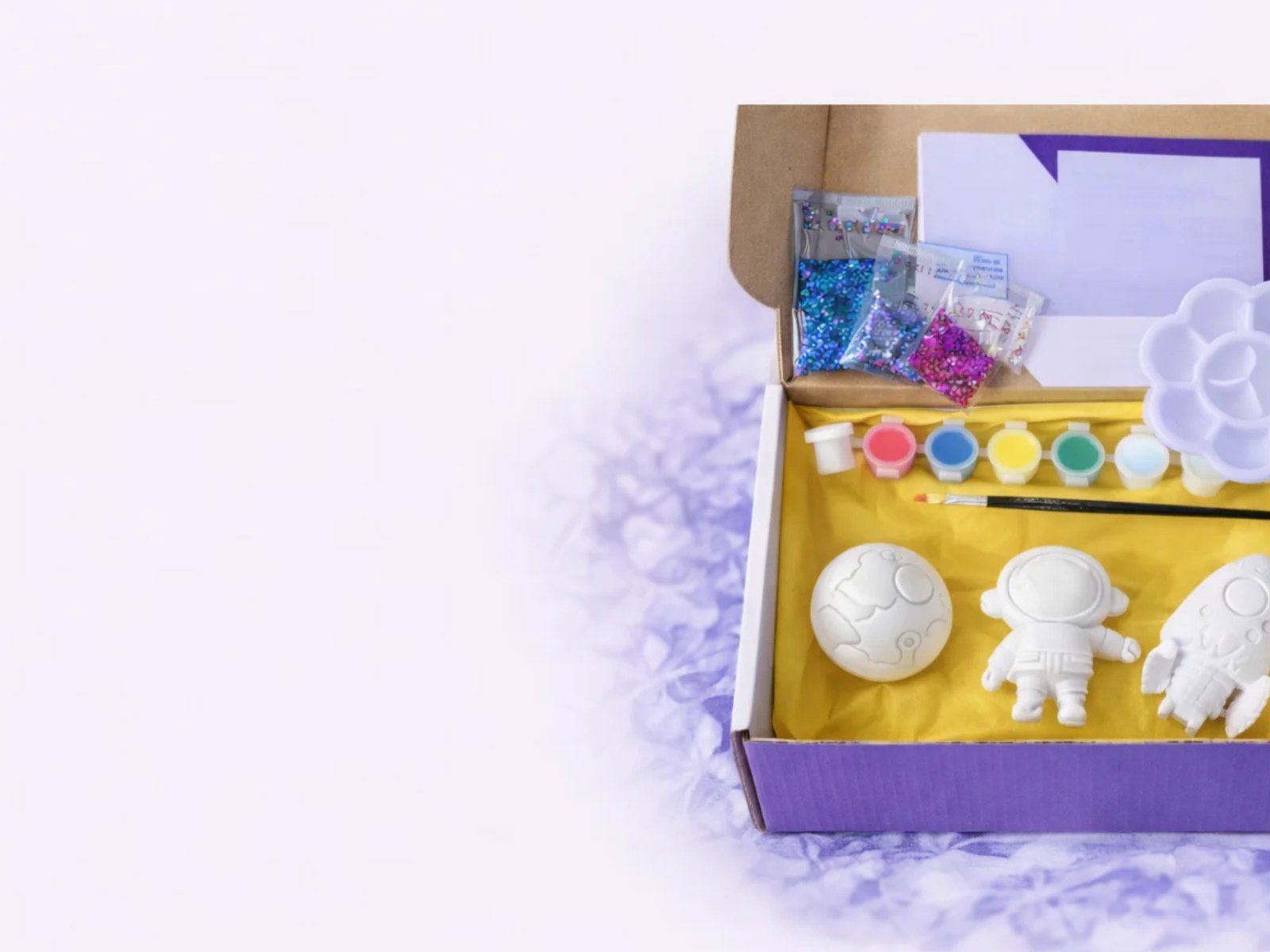 CREATIVE KITS
Paint your own space kit in a purple gift box with ceramic astronaut shapes, paints, glitter and brush on a soft lavender background