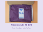 Purple tissue-wrapped package inside a cardboard box with a white OPEN ME label.