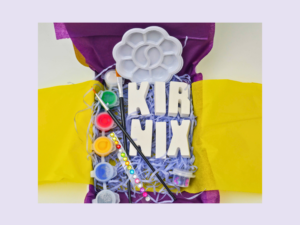 Colorful craft supplies on a purple and yellow backdrop, including a white flower-shaped paint palette, brushes, and paint pots.
