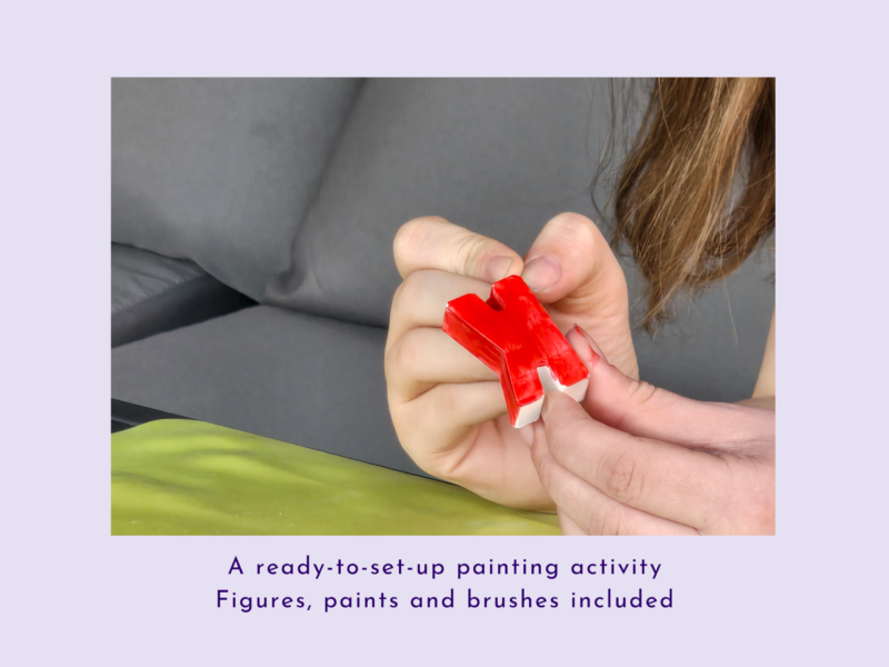 Close-up of hands tearing open red plastic wrapping on a craft item against a gray sofa backdrop.