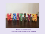 Colorfully painted wooden letters spelling 'HAPPY' arranged on a dark table with paint splatters on each letter.