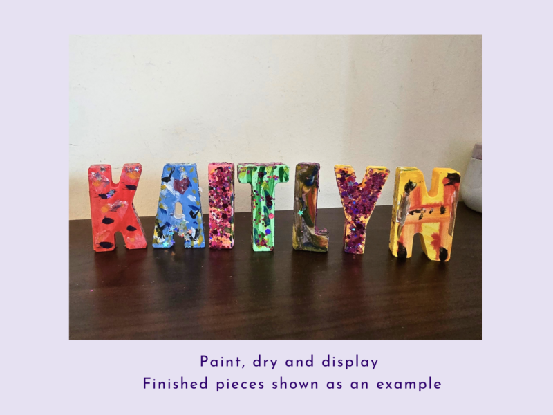 Colorfully painted wooden letters spelling 'HAPPY' arranged on a dark table with paint splatters on each letter.