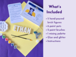 Flat lay of a craft kit on purple and yellow backgrounds: paint pots, brushes, glitter, and a circular paint palette, with a right-side lavender panel listing the kit contents.