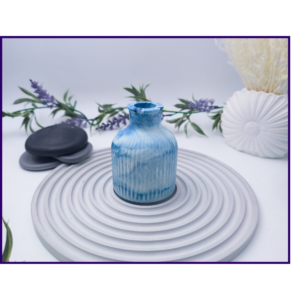 Decorative bud vase in blue and white marble shown on a striped surface beside black stones and neutral styling props