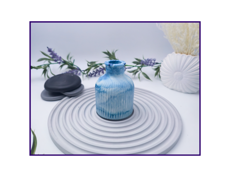 Decorative bud vase in blue and white marble shown on a striped surface beside black stones and neutral styling props