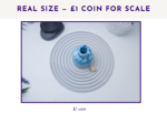 Poster announcing real size with a £1 coin for scale; photo shows a blue ceramic vase on a coiled cord with coins nearby.