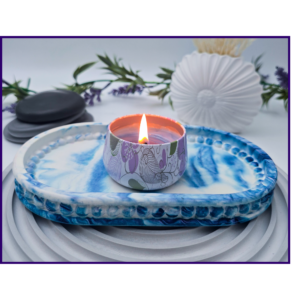 Lit candle in a patterned holder resting on a blue marbled plate with lavender and smooth stones in the background for decoration.