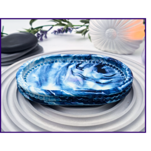 Small oval marbled tray on a striped surface beside black stones and dried stems