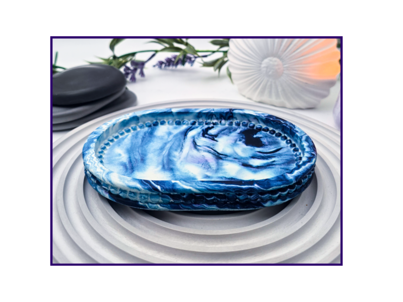 Small oval marbled tray on a striped surface beside black stones and dried stems
