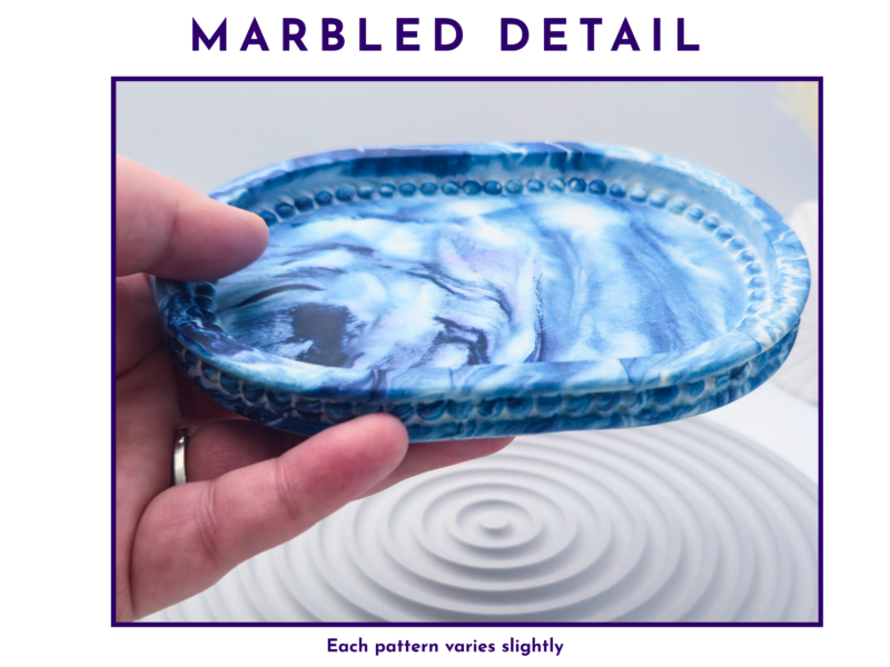 Hand holding the small oval tray close up to show the blue and white marbled detail