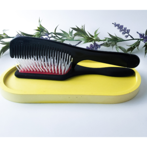 Black hairbrush resting on a yellow oval catchall tray with lavender stems in the background
