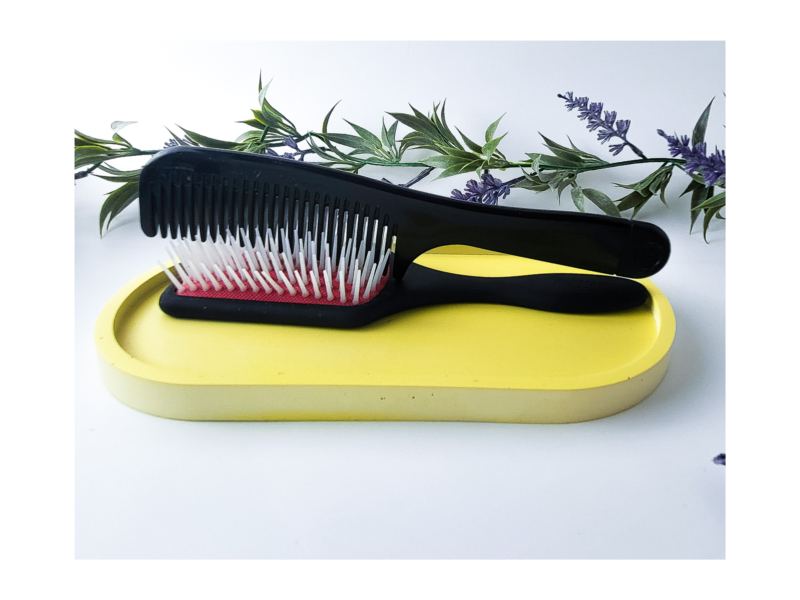 Black hairbrush resting on a yellow oval catchall tray with lavender stems in the background