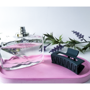Clear pink oval tray holding a black hairbrush on a pink surface with greenery behind
