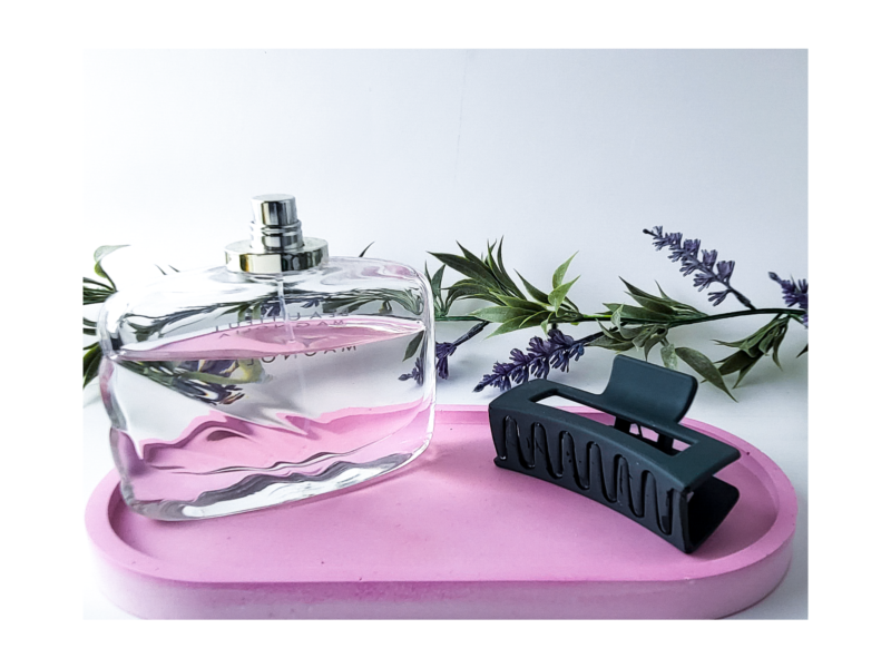Clear pink oval tray holding a black hairbrush on a pink surface with greenery behind